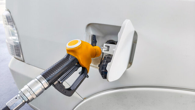 Fuel nozzle filling a white vehicle gas tank at a station. Transportation energy and automotive refueling process. Gasoline pump handle inserting into a car fuel port fuel crisis concept
