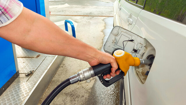 Man refueling white car at gas station. Gasoline pump nozzle inserting into vehicle fuel tank. Energy crisis and high fuel price concept. Transportation maintenance at petrol station