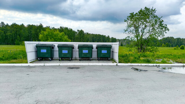 Four large green dumpsters standing at a roadside disposal site. Outdoor waste management containers located at a fuel station area. Environmental sanitation and cleaning concept