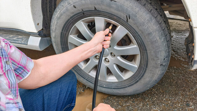 Man inflating car tire with air compressor hose at gas station. Automotive maintenance and vehicle safety check. Road travel preparation and tire pressure monitoring service concept