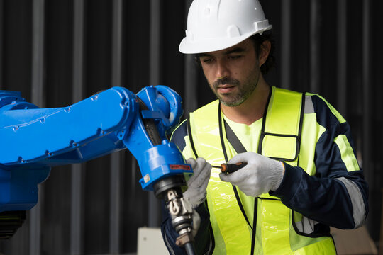 Male engineer wearing uniform, white hard hat and gloves repair automatic robotic arm for welding. Male technician inspecting quality automatic welding robot arm machine with hand tools