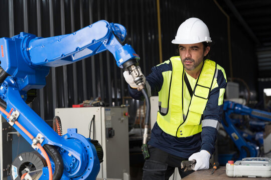 Male engineer wearing uniform, white hard hat and gloves repair automatic robotic arm for welding. Male technician inspecting quality automatic welding robot arm machine with hand tools