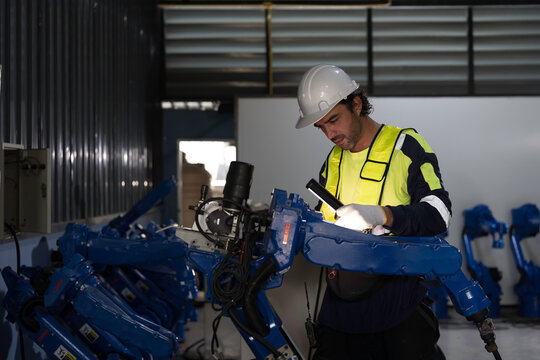 Male engineer wearing uniform, white hard hat and gloves repair automatic robotic arm for welding. Male technician inspecting quality automatic welding robot arm machine with hand tools
