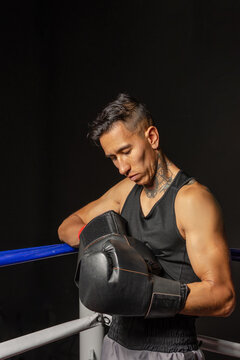 Young Hispanic boxer putting on gloves before training in dark gym