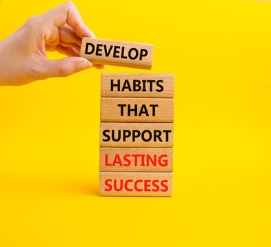 Concept words build habits that support lasting success on wooden blocks. Wooden block held above development block. Beautiful yellow background. Personal development concept. Copy space.