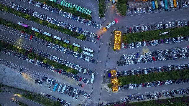 Aerial top-down view of a large crowded outdoor parking lot with rows of vehicles at dusk.