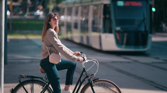 Video of pretty woman waiting for the tram to pass before crossing the street with her bicycle