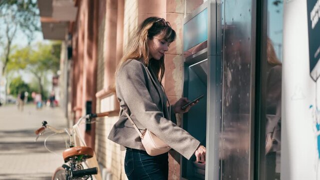 Video of beautiful woman withdrawing cash from an ATM using her smartphone in the city.