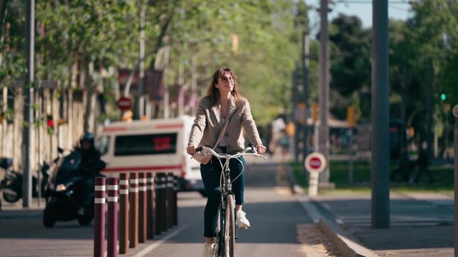 Video of smiling woman riding a bicycle in the bike lane through the city.