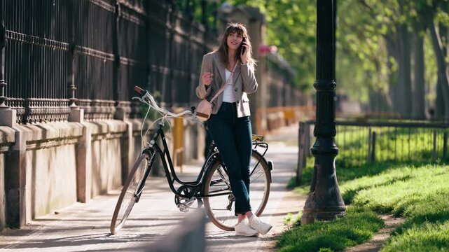 Video of beautiful woman talking on the phone while riding a bicycle through the park