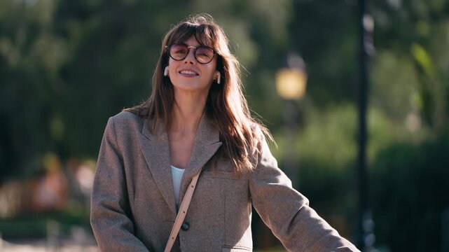 Video of happy woman listening to music with headphones while walking her bicycle through the park.