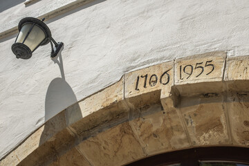 Untersicht Torbogen aus  Kalkstein mit Jahreszahl 1706 und 1955 an Mauer mit weißem Verputz und Laterne mit  Schlagschatten am Rathaus in Dettingen an der Erms © lebaer