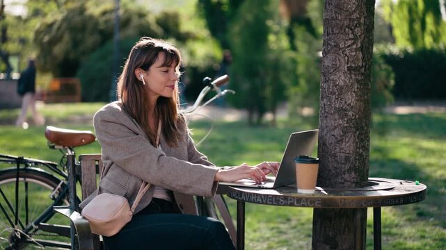 Video of beautiful woman listening to music with headphones while working on a laptop in the park.
