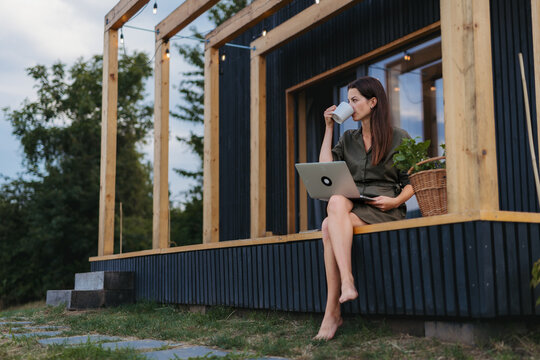Young woman sitting on tiny house patio, working on laptop.