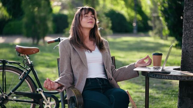 Video of beautiful woman doing ioga while working on a laptop in the park.