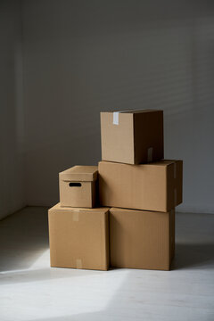 Vertical shot of stacked cardboard boxes standing in empty room, suggesting moving, storage, delivery, relocation concept. Ideal for logistics, home services, packing ads