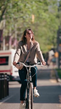 Video of smiling woman riding a bicycle in the bike lane through the city.