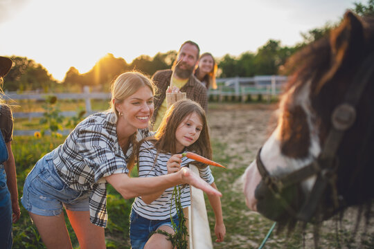Mother and daughter feeding horse during family visit to countryside farm.