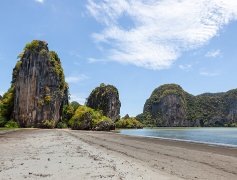 Rugged cliffs at Hat Ratcha Mongkhon beach, Sikao District, Trang, Thailand. Tropical coastline with sandy shore. Lush greenery and clear blue ocean.