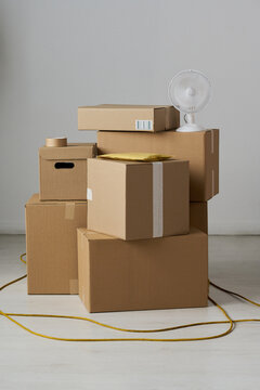 Vertical shot of stacked cardboard boxes, parcel mailer, packing tape, fan, extension cord suggesting home relocation, storage, shipping logistics. For moving service, delivery, decluttering ads
