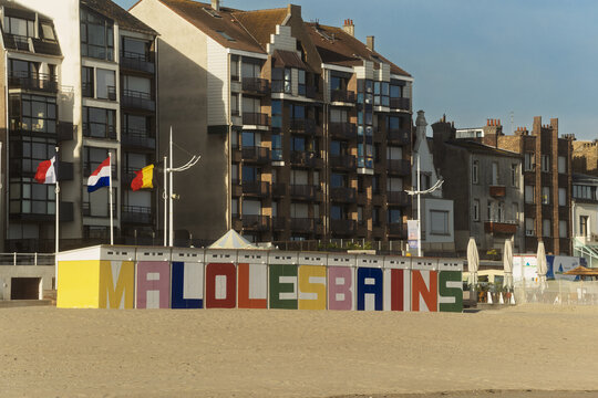 The Malo‑les‑Bains beach opens toward a row of tall seaside buildings, with bright letters and flags marking the lively Dunkirk shore.