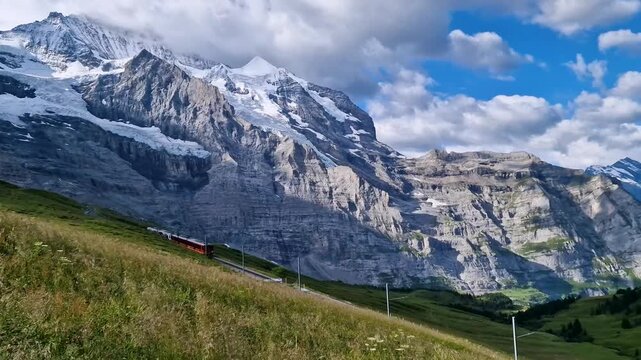 Red train Kleine Scheidegg Jungfrau region Switzerland 4K. Panoramic view of red mountain train passing green alpine meadows towards snowy peaks. Scenic Bernese Oberland travel b roll stock video