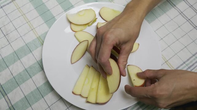 Hands of woman organizing red apple slices nicely around white plate - high shot