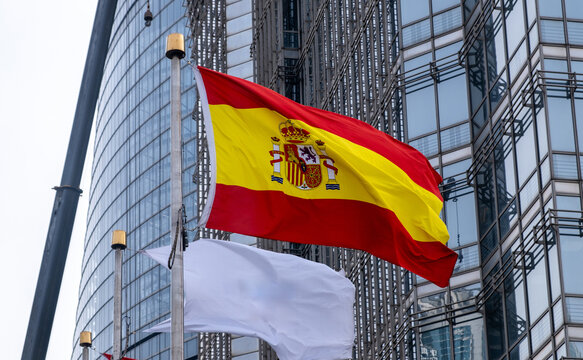 Spanish flag waving outside European Parliament in Brussels with glass facade and blue sky