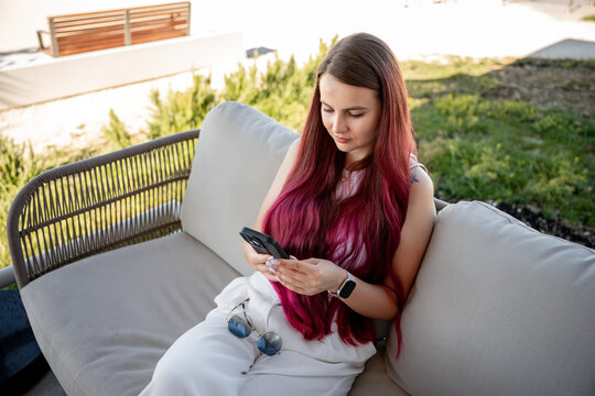 Young woman using smartphone on outdoor cafe sofa