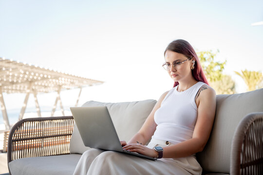 Focused woman working on laptop on outdoor seaside sofa