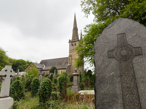 Historic St Paul's Church, Peel and graveyard with Celtic tombstone in Manchester UK, spire and weathered headstones in an overgrown churchyard