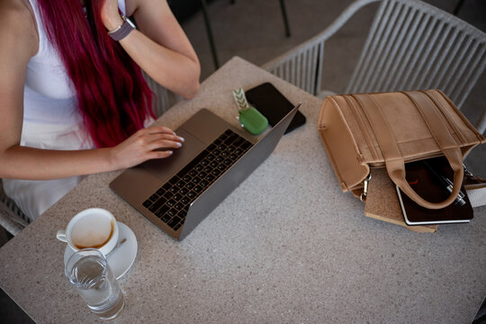 Woman using laptop at cafe table with coffee and bag