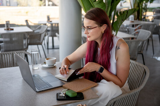 Young woman working on laptop and writing notes at cafe