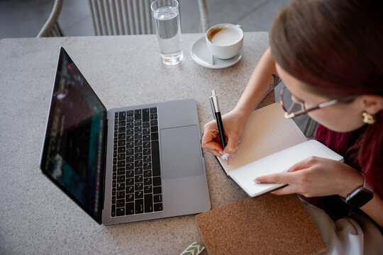 Woman taking notes beside laptop at cafe table workspace