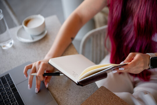 Woman writing notes with laptop and coffee at cafe table