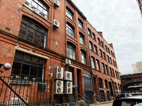Red brick industrial warehouse building with external air conditioning units, arched windows and metal doors in Manchester, UK urban street scene