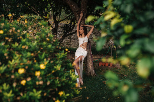 Young woman in white dress posing by tree in lush garden