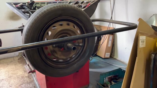 Close-up of a spinning car wheel mounted on a red balancing machine inside a garage. High-speed rotation during tire diagnostics or alignment process. Realistic auto service workshop environment.