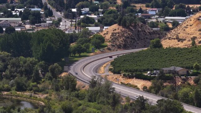 Aerial of highway US 2 passing through semirural valley Cashmere Washington with dry hillsides and coniferous forest patches in summer