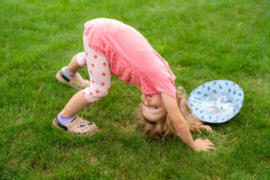 Little Girl Doing Bridge Stretch On Grass During Outdoor Summer Play And Active Childhood