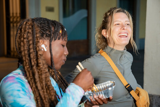 Gen Z woman friends eating takeaway and laughing outdoors