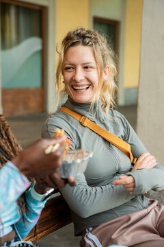 Smiling gen z woman chatting with friend on campus bench