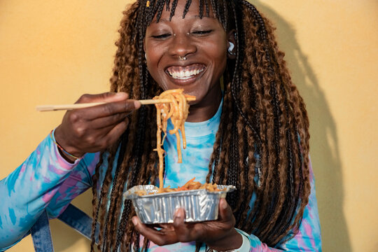 Gen Z woman enjoying takeout noodles with chopsticks