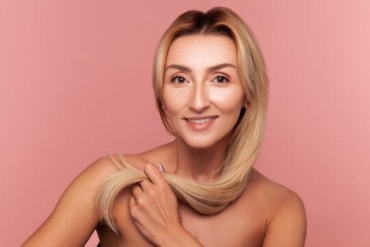 Cheerful woman showing her silky and strong hair strand for haircare products and shine demonstration isolated on pink background