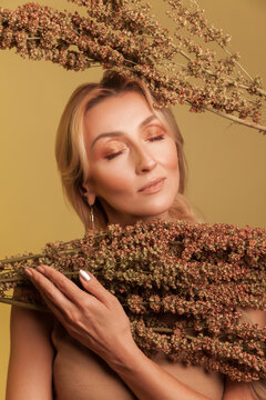 Serene blonde lady holding dried sorghum plants with eyes closed enjoying autumn atmosphere isolated over yellow background