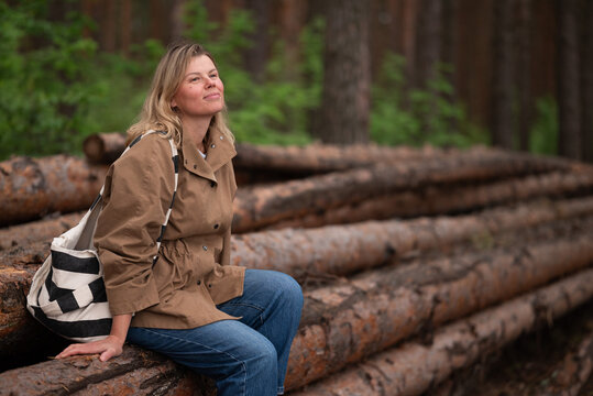 Woman resting on stacked logs in forest after a hike