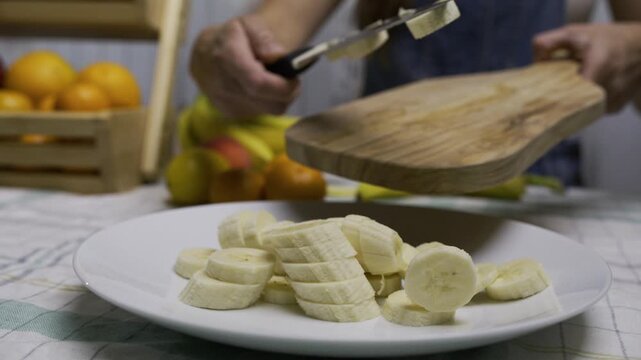 Woman using knife to scrape banana pieces onto plate - closeup, slow motion shot