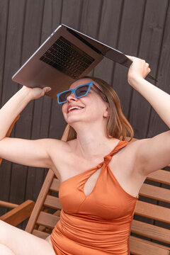 Woman in swimsuit holding laptop as shade outdoors