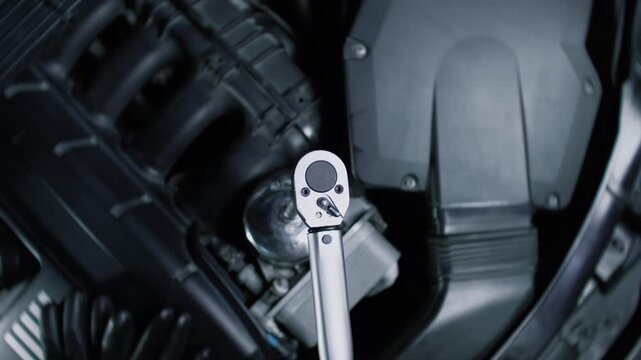 A torque wrench in operation under the hood of a racing car in a car service center. Close-up