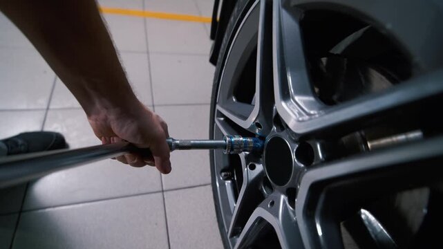 A mechanic at a tire shop loosens a car wheel using a large adjustable wrench.